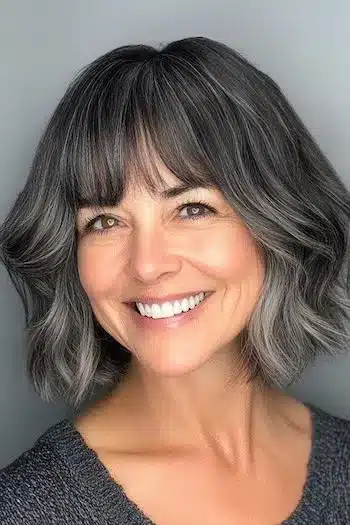 34 Sleek Bob Haircuts With Bangs That Feel Fresh and On-Trend 12 Salt and pepper wavy bob with bangs on a smiling woman, showcased in 34 Sleek Bob Haircuts With Bangs That Are Totally On-Trend.