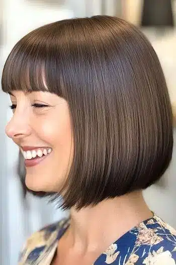 34 Sleek Bob Haircuts With Bangs That Feel Fresh and On-Trend 13 Blunt bob with straight bangs on a smiling woman, part of 34 Sleek Bob Haircuts With Bangs That Are Totally On-Trend.