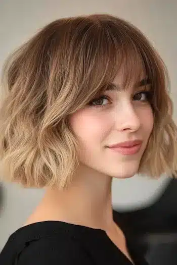34 Sleek Bob Haircuts With Bangs That Feel Fresh and On-Trend 3 Tousled wavy blunt bob with bangs on a woman, part of the 34 Sleek Bob Haircuts With Bangs That Are Totally On-Trend guide.